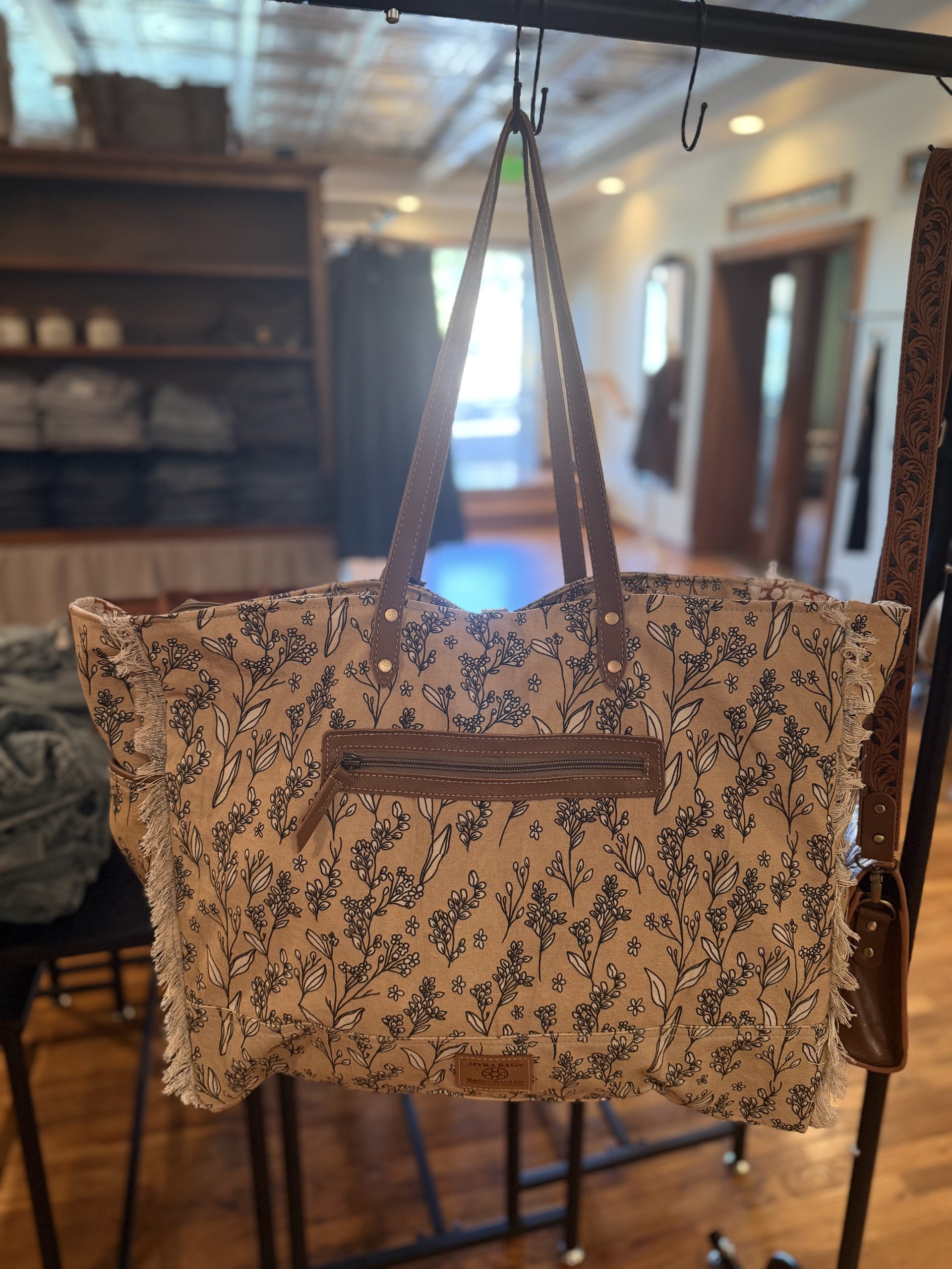 Tan wildflower print canvas tote with fringe edges and front zip pocket
