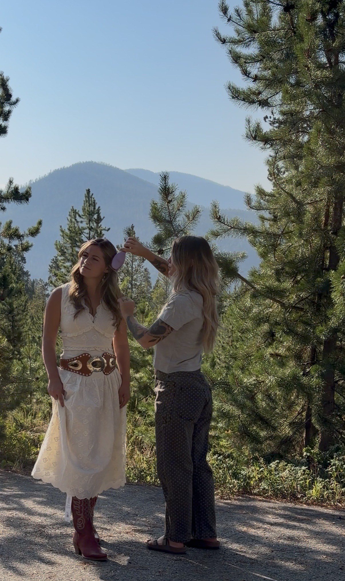 Two women standing at a mountain overlook with pine trees and Colorado mountains behind them