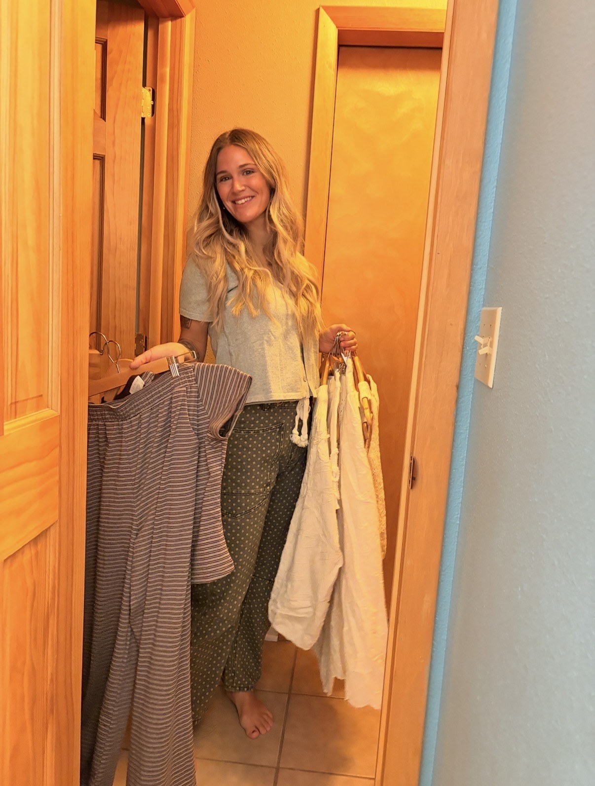 Amberly smiling in a doorway holding several garments on hangers