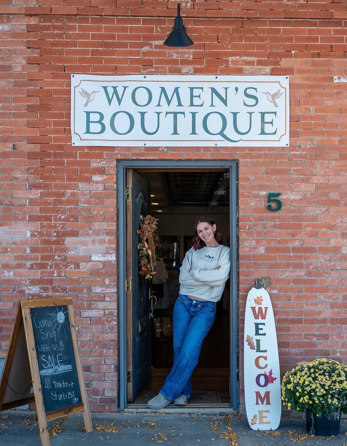 Amberly leaning in the open doorway of The Hummingbird Collective storefront in downtown Longmont