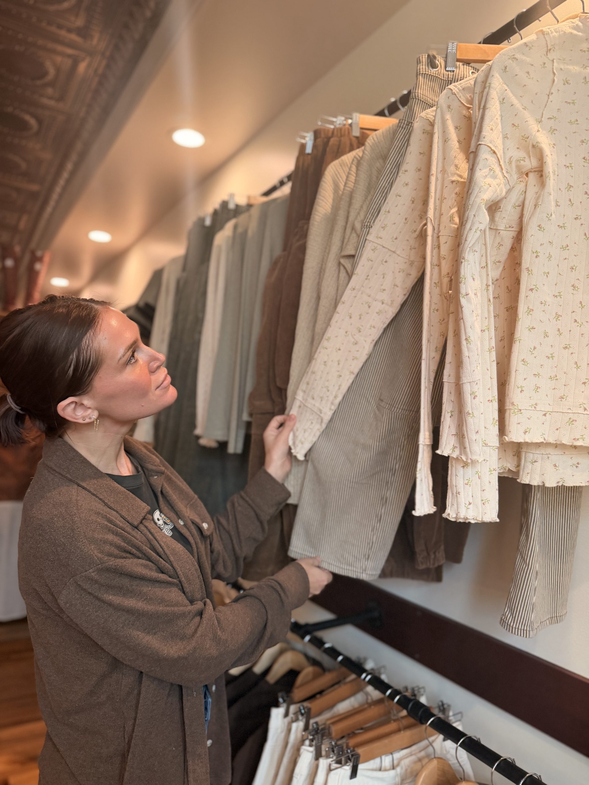 Amberly examines a floral top on a clothing rack inside The Hummingbird Collective.